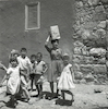 אשה מוקפת בילדים נושאת פח על ראשה.