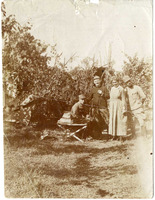 One soldier sits on camp bed outdoors, next to him two soldiers and a woman.