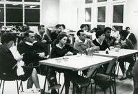 קבוצת אנשים יושבת סביב שולחנות באולם.