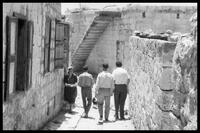 שלושה גברים הולכים בסמטה בין הבתים ולצדם אישה שהולכת בכיוון ההפוך.