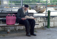An orthodox Jew taking a rest on a street banch, reading a newspaper.