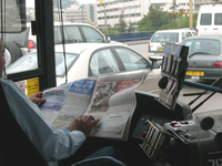 A bus driver reading a newspaper while he is driving the bus on the Tel Aviv Karlibach Street.