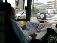 A bus driver reading a newspaper while he is driving the bus on the Tel Aviv Karlibach Street.