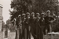 קבוצת גברים צעירים במדים וכובעי מלחים עומדים בחוץ.